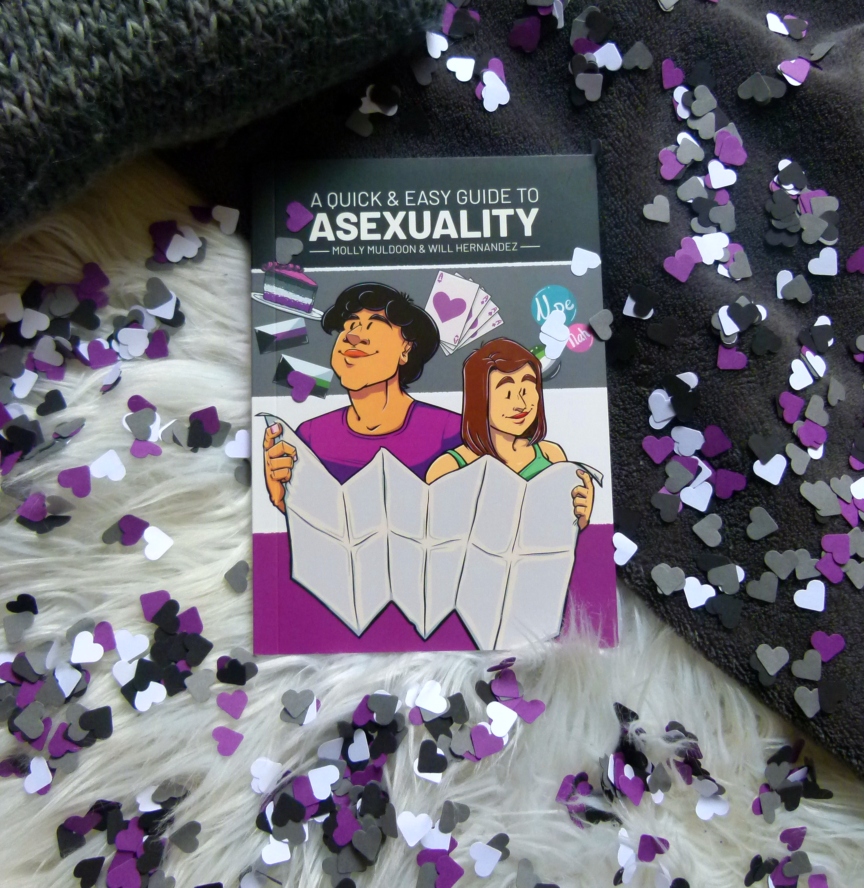 Das Buch liegt auf zwei verschiedenen Decken, weiß und schwarz. Um das Buch verteilt liegen unzählige ausgestanzte kleine Papierherzen in den Farben schwarz, grau, weiß und lila (der Asexuality-Flagge entsprechend).