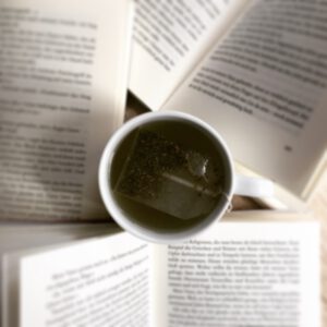 Im Foto ist eine Tasse von oben zu sehen, in der ein Teebeutel im Wasser schwimmt. Um das Buch herum liegen aufgeschlagene Bücher.