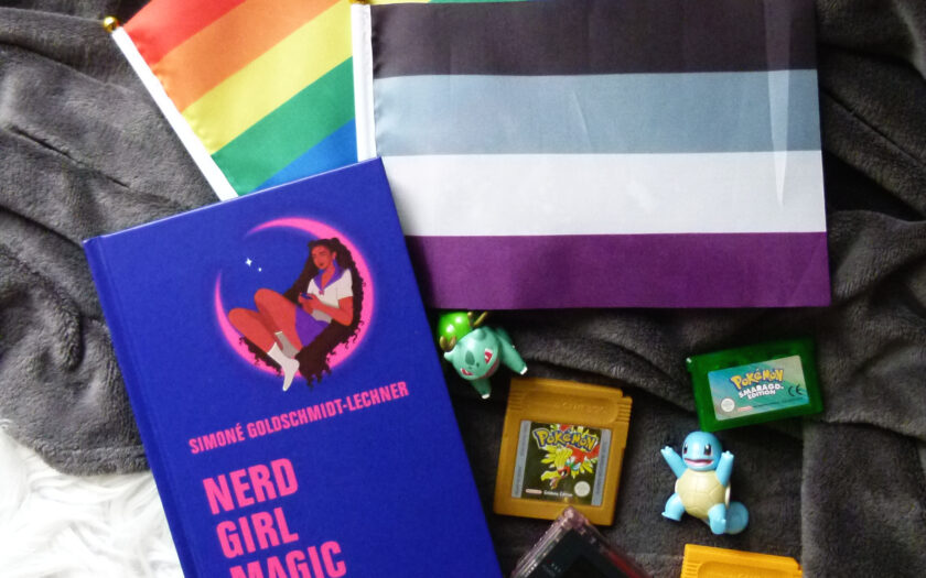 Das Foto zeigt das Sachbuch "Nerd Girl Magic" von Simoné Goldschmidt-Lechner umgeben von Pokémon-Figuren, Pokémon-Spielkartuschen, einem Gameboy Color und einer kleinen Regenbogen- und Ace-Flagge.
