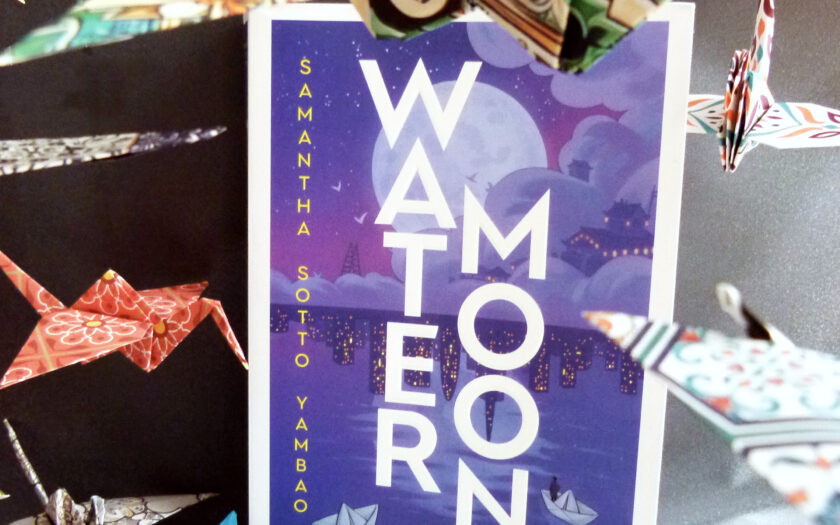 Das Foto zeigt den Roman Water Moon von Samantha Sotto Yambao auf einem dunklen Hintergrund. Um das Buch herum schweben Origami-Kraniche in bunten Farben.