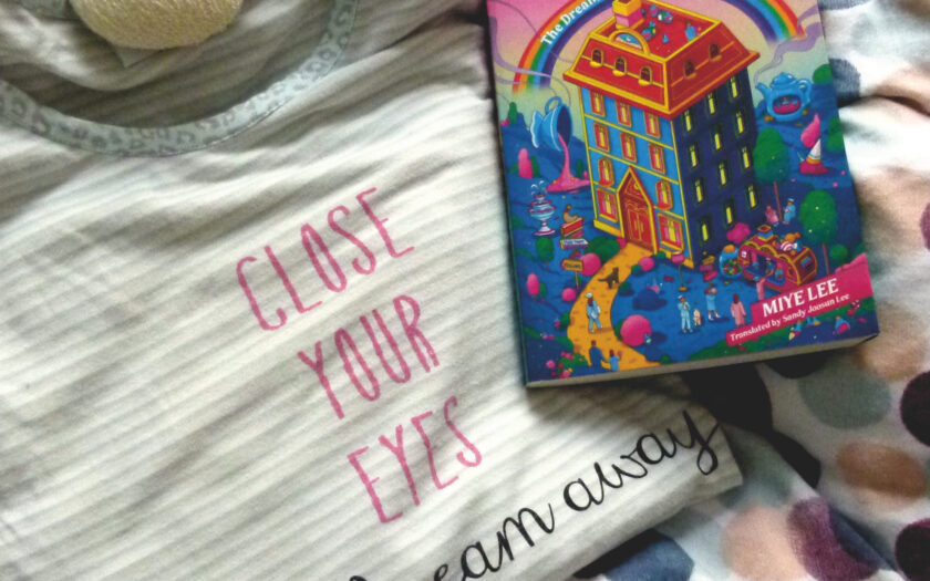 Das Buch liegt auf einer bunt gepunkteten Bettdecke und auf einem zusammengelegten Schlafanzugoberteil mit der Aufschrift "Close your eyes and dream away). Von oben ragt das Bein eines Plüschtiers ins Bild.