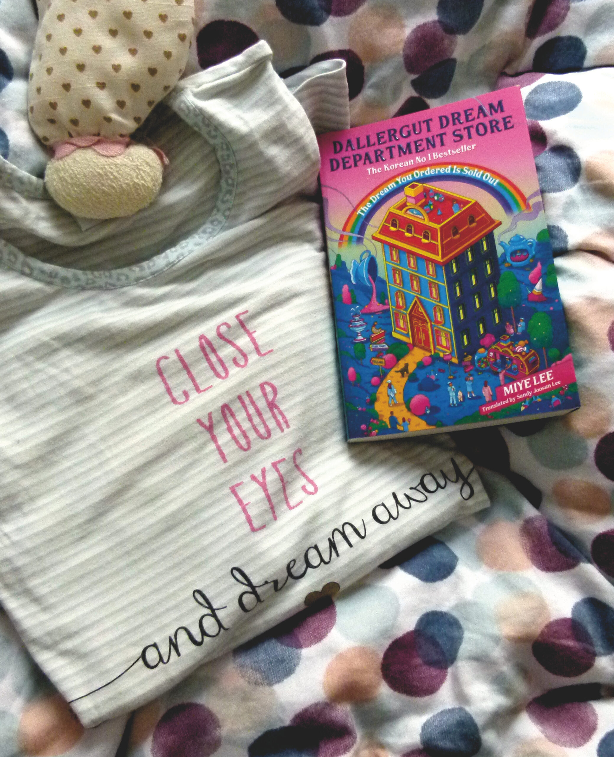 Das Buch liegt auf einer bunt gepunkteten Bettdecke und auf einem zusammengelegten Schlafanzugoberteil mit der Aufschrift