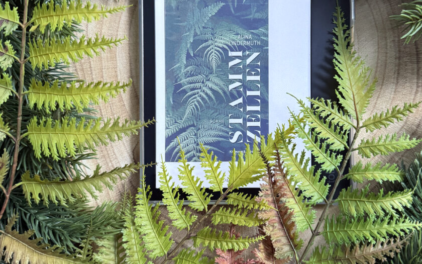 Der eReader mit dem farbigen Cover liegt auf einer Baumscheibe, umgeben von Farnen und Tannenzweigen (aus Plastik).