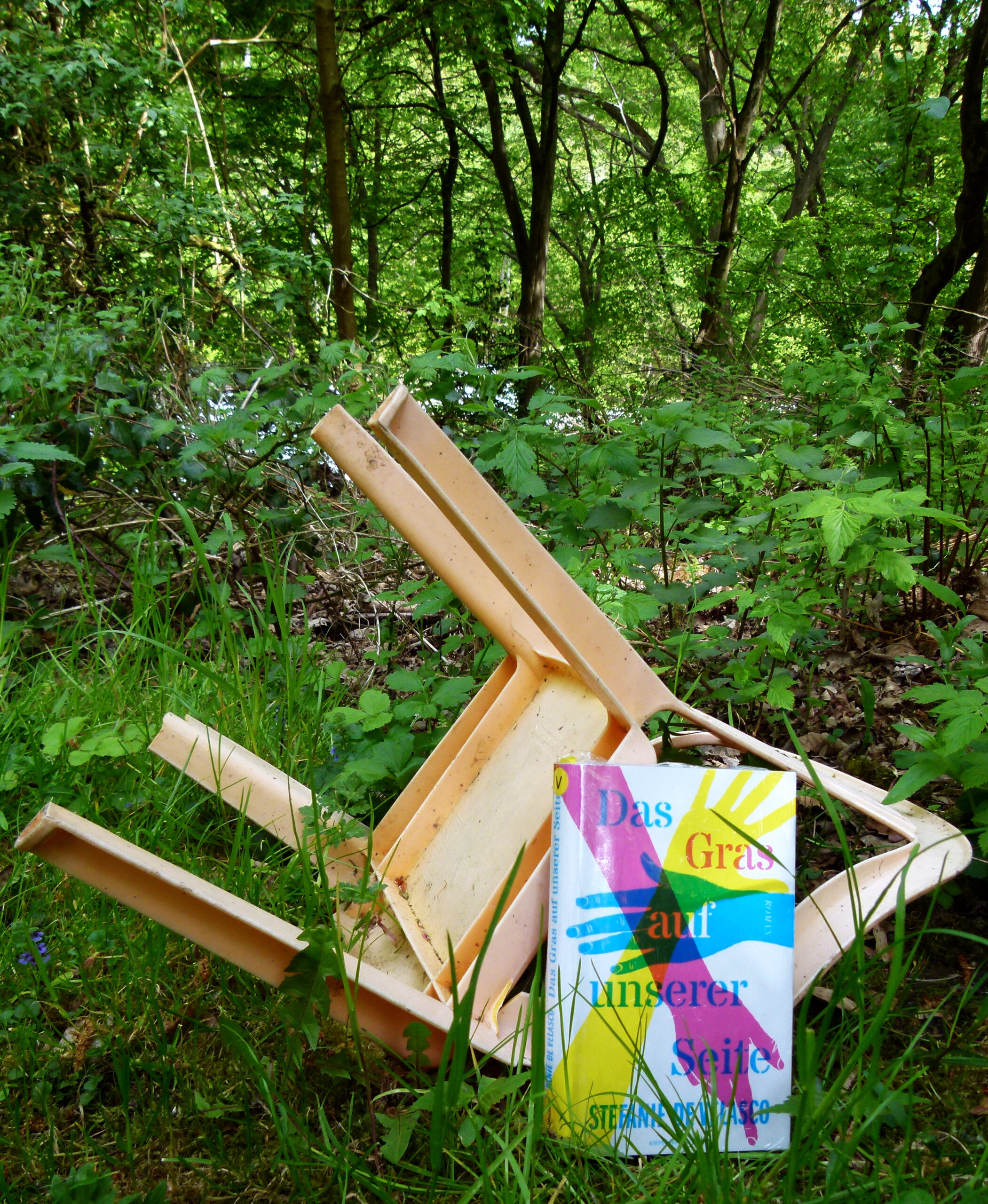 Das Buch steht im Wald an einen umgekippten, rosafarbenen Gartenstuhl gelehnt